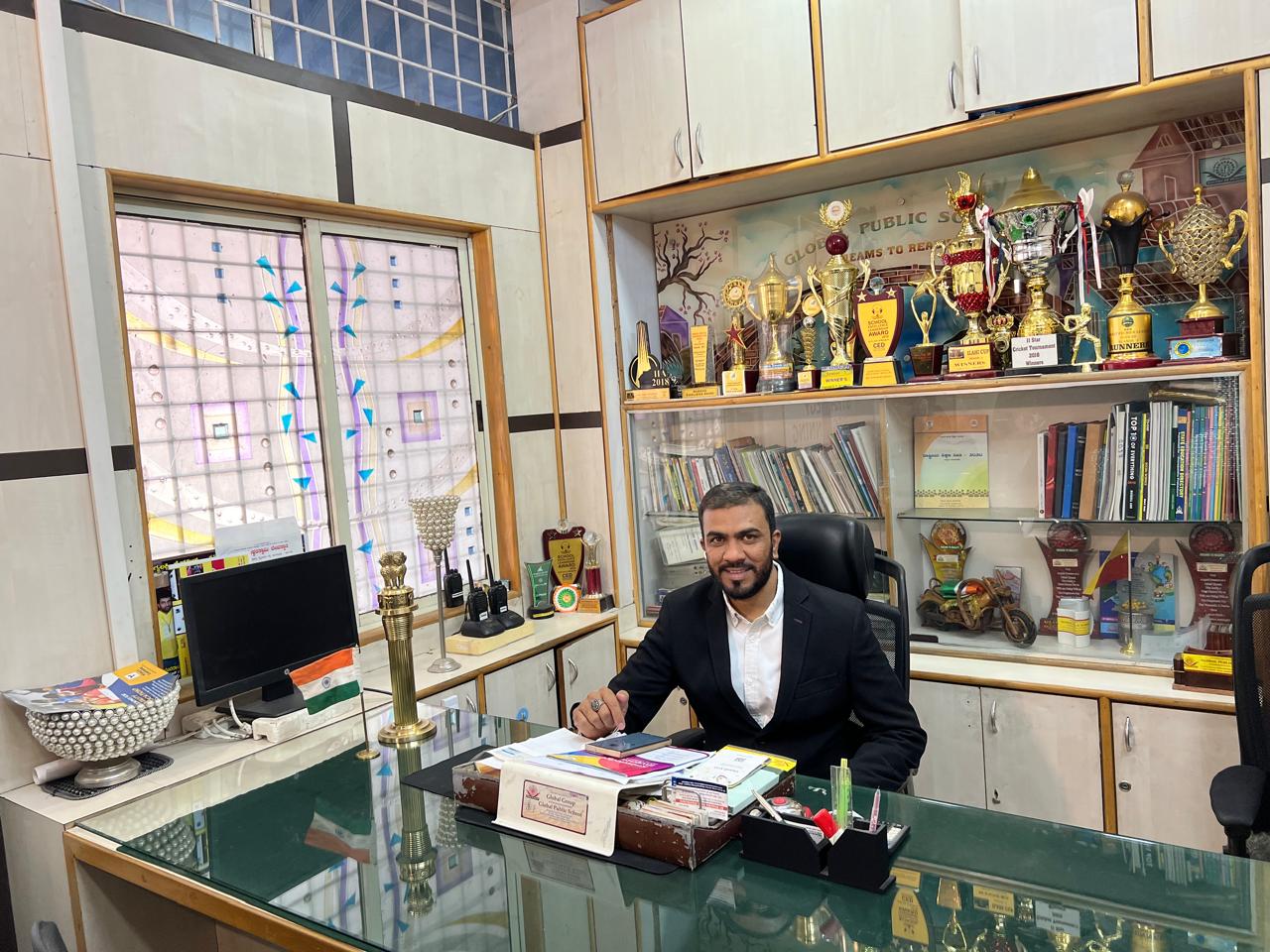 Principal seated at the office with trophies