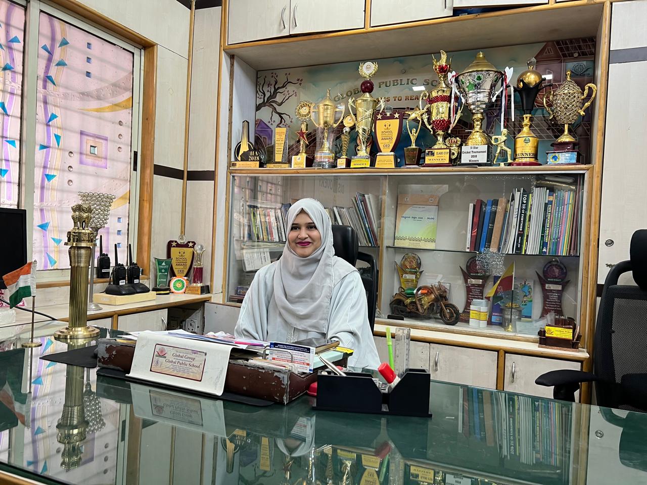 Principal seated at the office with a trophy cabinet